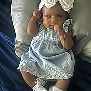 Nova is registered to the contest to win money with this photo: baby, infant, child, dress, headband, bow, socks, pillow, bed, blanket, sleepwear, cute, smile, skin, hand, footwear, lying_down, indoors, portrait, person