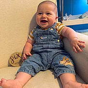 Ryder joined the competition — help win amazing prizes! baby, child, infant, denim_overalls, striped_shirt, smiling, sitting, chair, indoor, cute, happy, six_months, plush, barefoot, skin, face, person, blue_background, armrest, clothing