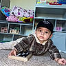 baby, child, toddler, portrait, indoors, carpet, sitting, lying_down, cap, plaid_shirt, collar, mamas_boy, wooden_board, letters, bookshelf, books, pillows, toys, home, cute