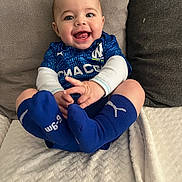 Marley participe au concours pour gagner de l'argent avec cette photo : baby, child, smiling, blue_clothing, socks, couch, blanket, happy, indoors, portrait, cute, infant, person, sitting, face, head, furniture, cozy, hands, feet