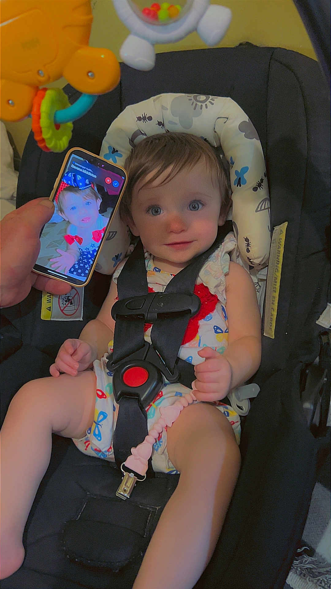Aurora is registered to the contest to win money with this photo: baby, car_seat, child, infant, phone, hand, toy, colorful, safety_harness, clothing, indoor, cute, portrait, expression, seat, pacifier_clip, face, person, looking, closeup