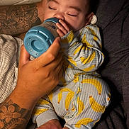 Damién is registered to the contest to win money with this photo: baby, sleeping, bottle, feeding, tattoo, hand, pajamas, banana_pattern, foot, cozy, bedtime, infant, person, closeup, skin, comfort, rest, cute, child, family