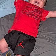 Joseph joined the competition — help win amazing prizes! baby, smiling, red_shirt, black_shorts, socks, smiley_face, bed, bedding, happy, infant, child, person, lying_down, indoors, casual_clothing, cute, small, joyful, raised_arms, head