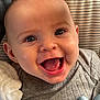 Silas is registered to the contest to win money with this photo: baby, smiling, close_up, face, child, infant, happy, gray_clothing, blanket, teether, cushion, striped_background, cute, young_child, portrait, skin, eyes, mouth, tongue, indoor