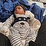 baby, infant, bed, blanket, clothing, onesie, hat, mittens, bottle, furniture, interior, person, laying, striped_clothing, black_hat, white_mittens, baby_bottle, indoors, calm, young_child