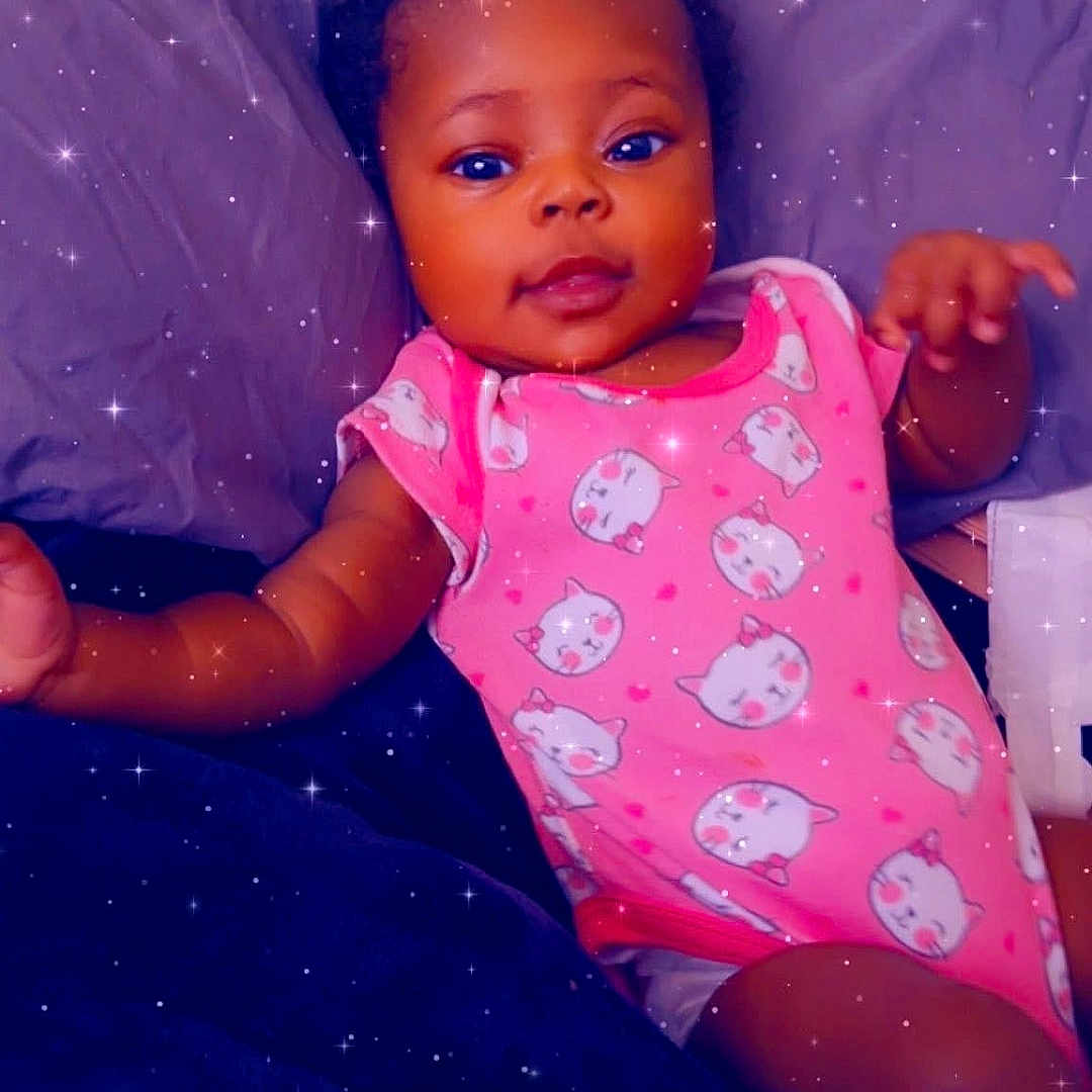 Harmony Chanel is registered to the contest to win money with this photo: baby, infant, pink_onesie, cat_prints, bed, pillow, sparkle_filter, child, cute, smiling, lying_down, indoors, person, young_child, face, expression, curious, skin, hand, head