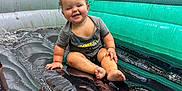 Bailey is registered to the contest to win money with this photo: toddler, child, smiling, wet, inflatable, bounce_house, playful, outdoor, summer, fun, happy, reflection, greenery, shirt, barefoot, sitting, water, mesh_window, plastic, inflatable_floor