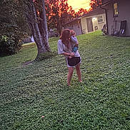 Bailey is registered to the contest to win money with this photo: child, person, grass, tree, sunset, house, outdoor, nature, sky, greenery, holding, baby, silhouette, twilight, yard, evening, casual_clothing, shoes, warm_light, love