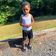 Jayvier is registered to the contest to win money with this photo: child, boy, toddler, outdoor, portrait, standing, forest, trees, grass, sunlight, summer, white_tank_top, black_shorts, sneakers, gravel, wood, nature, park, face, full_body