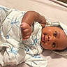newborn, baby, infant, child, face, eyes, swaddled, blanket, hospital, bed, portrait, lying_down, raised_fist, cozy, indoors, bedding, brown_skin, dark_hair, wide_eyes, photography