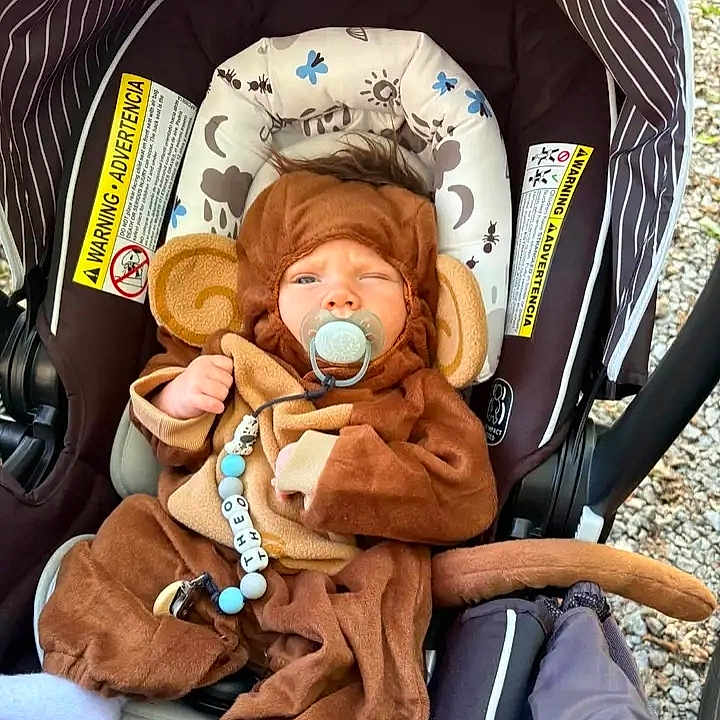 Ryker joined the competition — help win amazing prizes! baby, infant, child, stroller, monkey_costume, animal_costume, pacifier, sitting, buckled_in, brown_clothing, hat, tail, toy, baby_carrier, outdoor, pebbles, portrait, face, playful, family_photo