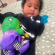 Zyair joined the competition — help win amazing prizes! baby, infant, stuffed_toy, toy, pacifier, pillow, curly_hair, black_clothing, indoor, floor, wooden_floor, plush_toy, green_toy, purple_toy, striped_socks, child, person, cute, resting, cozy
