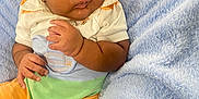 Zyair is registered to the contest to win money with this photo: baby, infant, curly_hair, blanket, blue_blanket, orange_shorts, white_shirt, colorful_clothing, cute, indoors, soft_texture, portrait, child, skin, person, young_child, resting, looking_sideways, cozy, casual_clothing