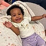 baby, smiling, infant, blanket, purple_pants, white_shirt, fairy_print, happy, cute, child, indoor, cozy, soft_texture, patterned_blanket, relaxed, portrait, person, arms_outstretched, curly_hair, comfortable