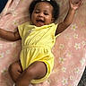 baby, child, infant, yellow_outfit, pink_blanket, curly_hair, white_bow, smiling, happy, soft_texture, lying_down, cute, adorable, playful, indoors, cozy, socks, small_arms, cheerful, portrait