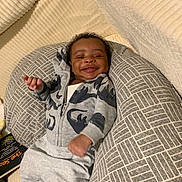 Kazai is registered to the contest to win money with this photo: baby, blanket, child, clothing, comfortable, cozy, cushion, cute, dinosaur, happy, hoodie, indoors, infant, pattern, person, portrait, relaxing, resting, smiling, young