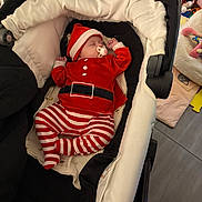 Maëlys participe au concours pour gagner de l'argent avec cette photo : baby, infant, sleeping, stroller, red_clothing, striped_pants, pacifier, hat, indoor, toys, blanket, cushion, floor, baby_bedding, child, person, cute, resting, holiday_outfit, nursery