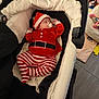 baby, infant, sleeping, stroller, red_clothing, striped_pants, pacifier, hat, indoor, toys, blanket, cushion, floor, baby_bedding, child, person, cute, resting, holiday_outfit, nursery