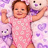 baby, blanket, child, curly_hair, cute, heart_pattern, indoor, infant, lying_down, medical_tube, nursery, pastel, pink, pink_bow, pink_outfit, portrait, purple, smiling, stuffed_animal, teddy_bear