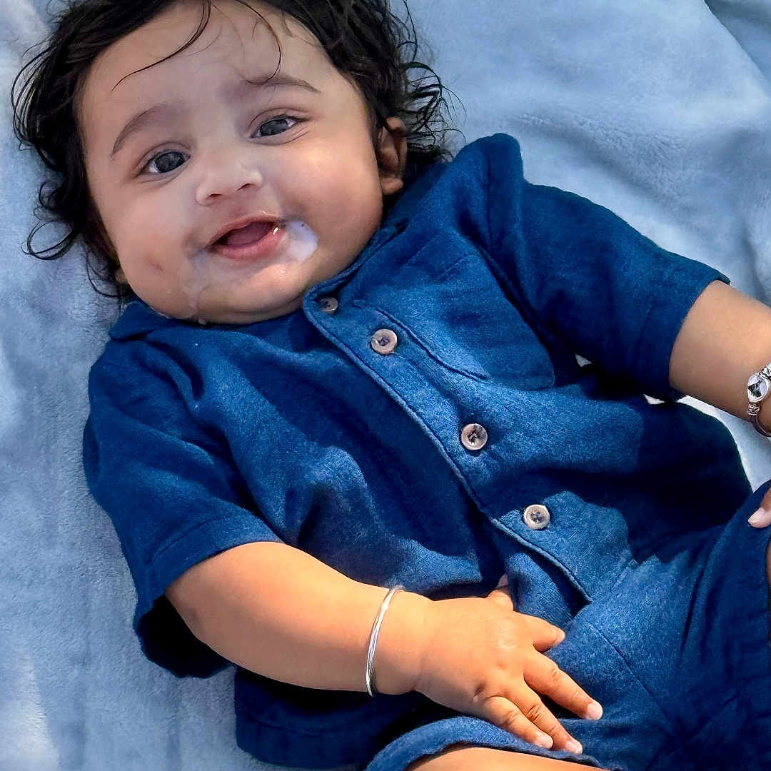 Shaurya is registered to the contest to win money with this photo: baby, blanket, blue_outfit, bracelet, child, curly_hair, cute, dimples, drool, face, hand, happy, infant, lying_down, outdoor, portrait, skin, smiling, soft_texture, young_child
