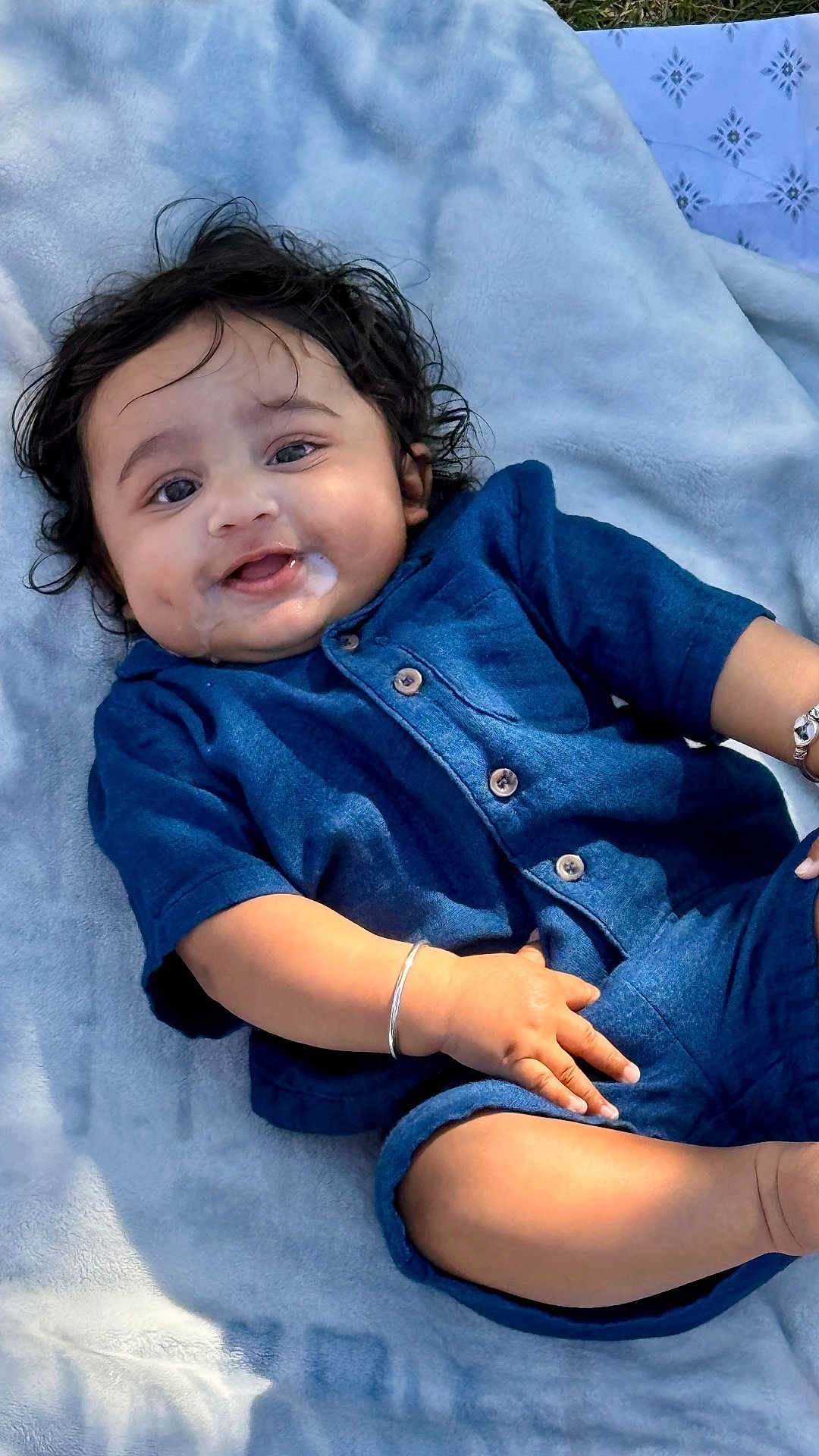 Shaurya is registered to the contest to win money with this photo: baby, infant, child, blue_outfit, bracelet, curly_hair, dimples, drool, blanket, smiling, happy, cute, portrait, young_child, lying_down, skin, face, hand, outdoor, soft_texture