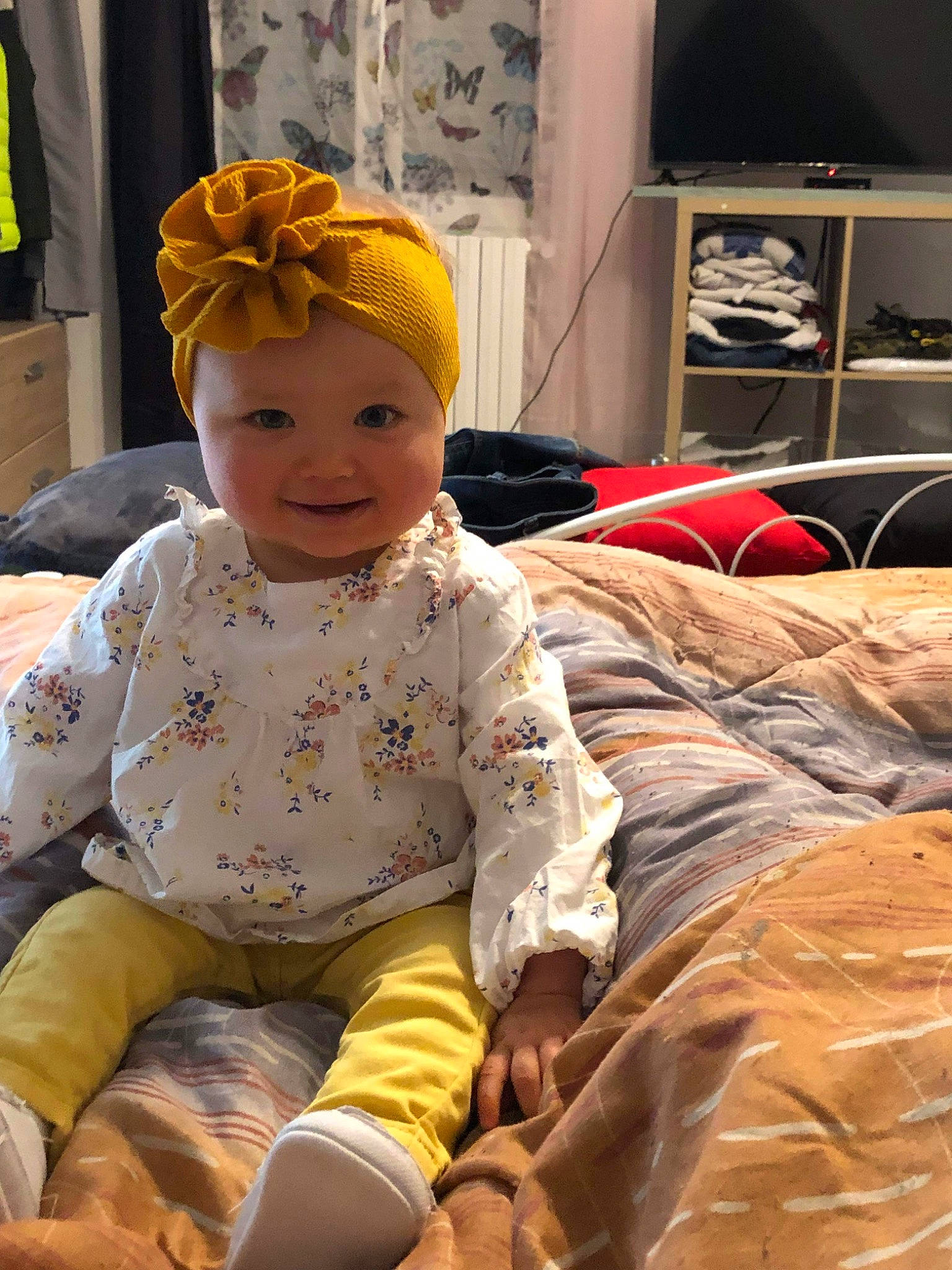 Léonie participe au concours pour gagner de l'argent avec cette photo : baby, baby_laughing, baby_products, baby_toddler_clothing, beanie, child, comfort, flooring, fun, happy, headgear, headwear, linens, person, room, sitting, skin, smile, television, textile
