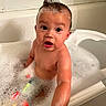 baby, child, infant, bath, bathtub, bubble_bath, foam, water, wet, hair, soap, bath_toy, colorful_toys, portrait, sitting, indoors, bathroom, smiling, surprised, close_up