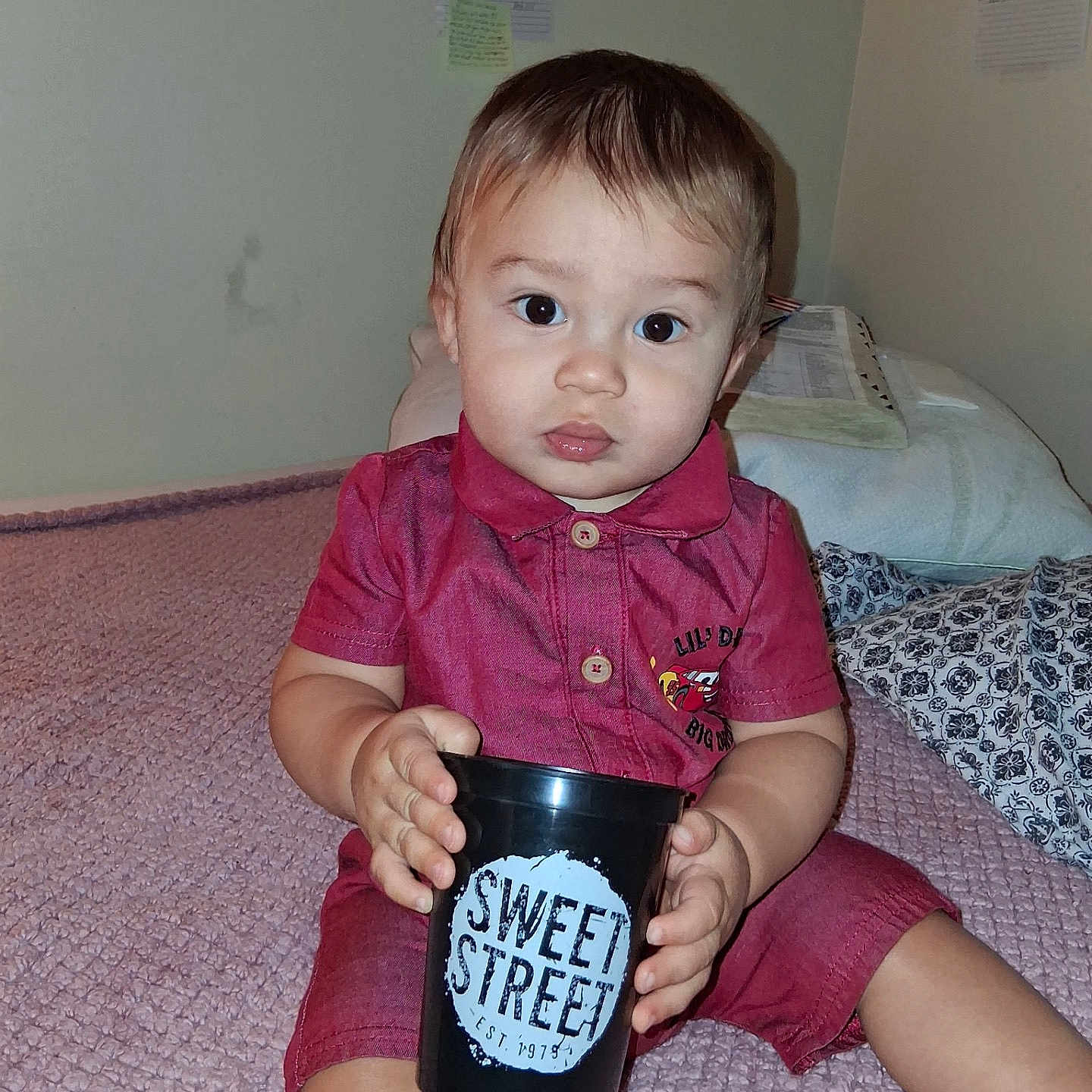 Azriel joined the competition — help win amazing prizes! baby, child, infant, portrait, sitting, bed, blanket, pillow, indoors, home, pink_clothing, romper, cup, black_cup, sweet_street, text, hands, brown_hair, wide_eyes, smiling
