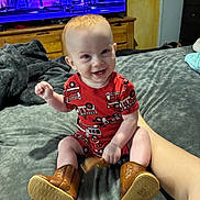 Dino joined the competition — help win amazing prizes! baby, bed, blanket, boots, child, clothing, cute, fire_truck_pattern, footwear, furniture, happy, home, indoor, person, red_hair, room, sitting, smiling, television, toy