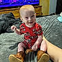 baby, bed, blanket, boots, child, clothing, cute, fire_truck_pattern, footwear, furniture, happy, home, indoor, person, red_hair, room, sitting, smiling, television, toy