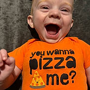 Dino is registered to the contest to win money with this photo: baby, child, smiling, orange_shirt, text_on_clothing, happy, face, head, infant, cute, playful, portrait, toddler, person, clothing, expression, indoor, closeup, joyful, casual