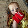 baby, infant, boxing_glove, red, striped_blanket, tiger_pattern, yellow_clothing, chewing, lying_down, blue_eyes, cute, child, playful, indoors, closeup, soft_lighting, fabric, hand, face, expression