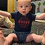 arms, baby, bed, bedroom, child, clothing, denim_shorts, door, expression, eyes, face, furniture, indoor, infant, legs, mouth, navy_shirt, person, tattoo, text_on_clothing