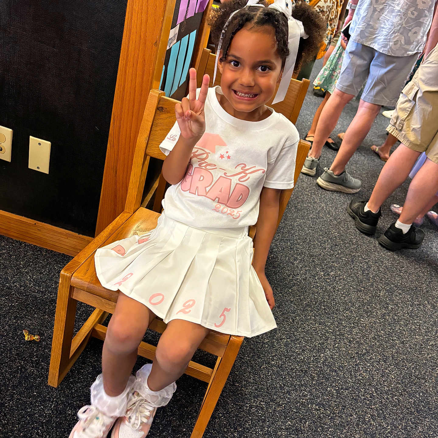 Lamariah is registered to the contest to win money with this photo: background, carpet, celebration, chair, child, crowd, event, girl, graduation, hair_bows, happy, indoor, peace_sign, people, person, pleated_skirt, smiling, sneakers, white_clothing, wood