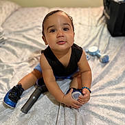 Aiden is registered to the contest to win money with this photo: toddler, child, baby, indoor, bed, toy, sitting, curious, black_clothing, blue_shoes, bracelet, person, face, expression, home, patterned_bedspread, soft_focus, small_object, floor, room