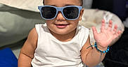 Aiden joined the competition — help win amazing prizes! toddler, child, sunglasses, smile, wave, white_tank_top, blue_shorts, bracelet, brush, bed, pillow, shoes, indoor, cute, happy, baby, person, casual, accessory, playful