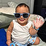 toddler, child, sunglasses, smile, wave, white_tank_top, blue_shorts, bracelet, brush, bed, pillow, shoes, indoor, cute, happy, baby, person, casual, accessory, playful