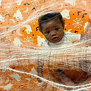 Zymir Coats joined the competition — help win amazing prizes! baby, child, infant, portrait, face, eyes, curious, halloween, spider, cobweb, ghosts, orange, blanket, costume, indoors, lying_down, photography, cute, holiday, patterned_background