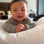 Koda is registered to the contest to win money with this photo: baby, infant, smile, chubby_cheeks, hands, pillow, bed, blanket, onesie, portrait, face, eyes, mouth, indoor, cozy, cute, happy, clothing, room, parenting