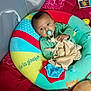 baby, pacifier, cushion, toy, plush, red_blanket, child, indoor, comfort, sleeping_area, soft_toys, colorful, green_clothing, infant, resting, cute, cozy, nursery, playtime, relaxation