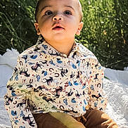 Kolson is registered to the contest to win money with this photo: toddler, child, outdoor, grass, blanket, shirt, patterned_clothing, brown_pants, socks, sitting, sunlight, face, curious, young_child, portrait, nature, baby, cute, daylight, expression