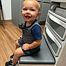 toddler, child, smiling, portrait, indoor, laundry_room, washing_machine, appliance, seated, blue_clothing, shorts, sneakers, wood_floor, home, kitchen, happy, face, blond_hair, full_body, photograph