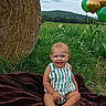 baby, child, smiling, outdoor, portrait, farmland, corn_field, hay_bale, balloons, greenery, grass, hills, sky, clouds, blanket, seated, striped_clothing, overalls, barefoot, rural_landscape