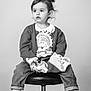 toddler, child, jeans, cardigan, sneakers, shirt, stool, black_and_white, portrait, indoor, curly_hair, casual_clothing, footwear, sitting, young_child, expression, curious, studio, fashion, cute