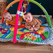 Lëya a rejoint le concours — aidez-le/la à gagner de superbes lots ! baby, infant, twin_babies, play_mat, play_gym, toy, colorful, crawling, indoor, wooden_floor, sweater, pacifier, face, looking_at_camera, mat, basket, denim_pants, cute, smiling, floor_rug