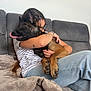 Hera participe au concours pour gagner de l'argent avec cette photo : dog, person, hugging, couch, blanket, glasses, striped_shirt, jeans, tattoo, living_room, pet, indoor, comfort, canine, affection, paw, fur, relaxation, home, tongue