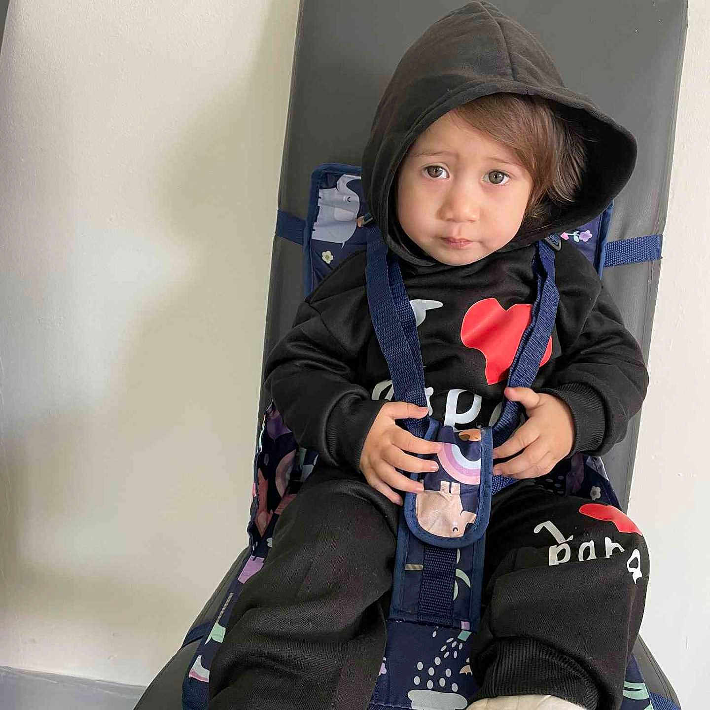 Hia'Ai a rejoint le concours — aidez-le/la à gagner de superbes lots ! baby_seat, black_clothing, casual, chair, child, curious, expression, floor, footwear, home, hoodie, indoor, patterned_fabric, person, portrait, sitting, straps, toddler, white_socks, young_child