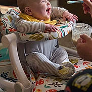 Ezra joined the competition — help win amazing prizes! baby, bib, closeup, cute, eye_contact, feeding, food, hands, highchair, home_interior, infant, jar, laughing, onesie, parent_hand, patterned_fabric, play_seat, smile, socks, spoon