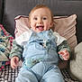 baby, child, smiling, denim_overalls, pacifier, couch, pillow, blanket, indoor, happy, cute, sitting, person, clothing, footwear, face, head, young_child, comfortable, home