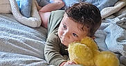 Waylon joined the competition — help win amazing prizes! toddler, child, baby_bottle, blanket, bed, plush_toy, stuffed_animal, yellow_chicks, soft_toys, indoor, cozy, curly_hair, laying_down, cute, young_child, comfort, resting, playful, home, nap_time